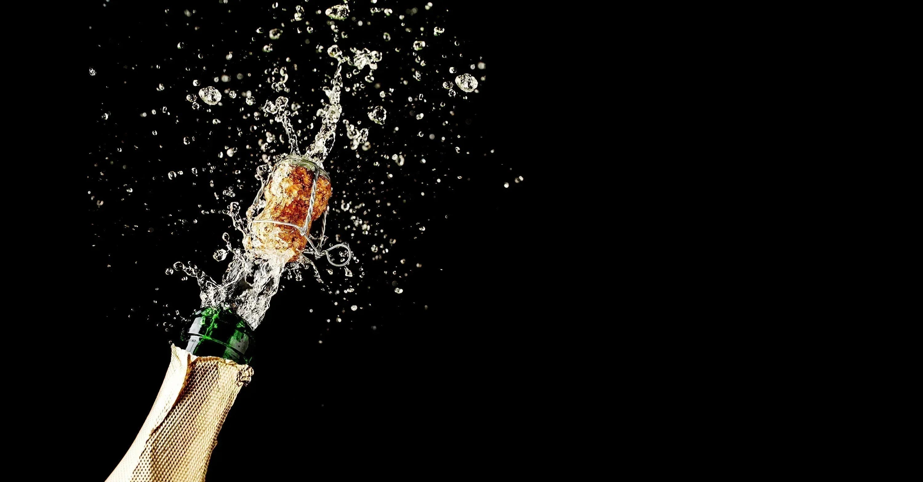 Champagne cork popping mid-air with an explosive spray of bubbles against a black background.