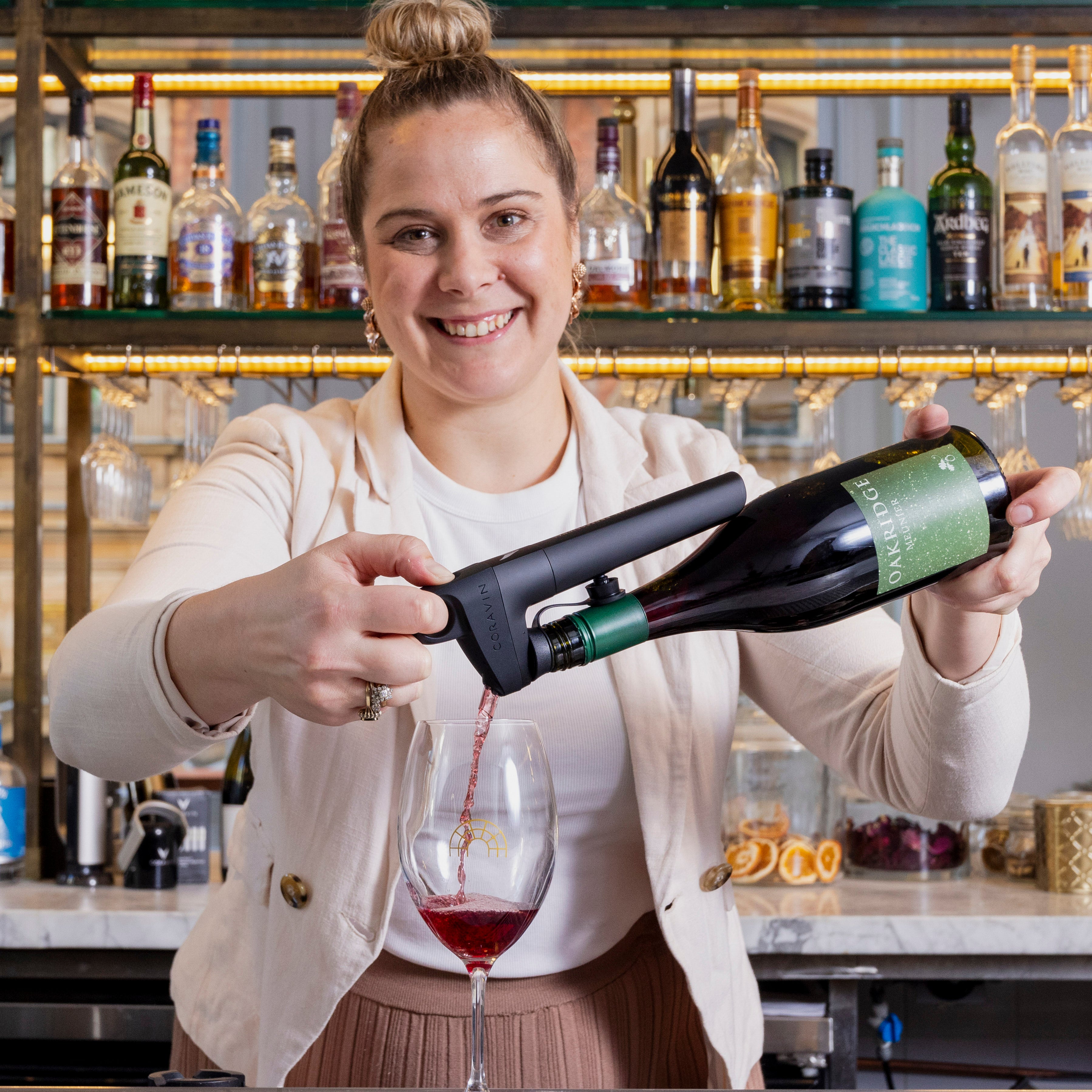 Bartender pouring red wine from a bottle into a glass, with a variety of liquor bottles displayed in the background.